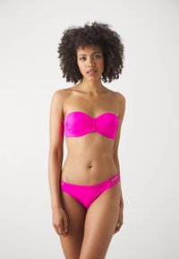 Biquíni rosa brilhante com parte de cima tipo bandeau com detalhe franzido e parte de baixo combinando com recortes e tiras laterais. Textura suave.