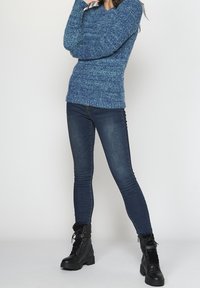 Pull en tricot bleu avec un design texturé, associé à un jean skinny bleu foncé et des bottines noires à lacets avec un motif en fausse fourrure.