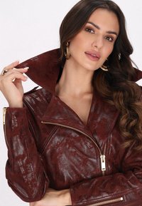 Burgundowa kurtka z sztucznej skóry o teksturowanym wykończeniu, z oversize'owym kołnierzem, zapięciem na zamek błyskawiczny i złotymi akcentami.