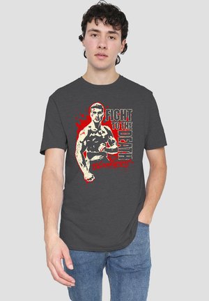Young man wearing a dark gray T-shirt with a graphic of a muscular fighter and the text "Fight to the Death Bloodsport" in red and white.