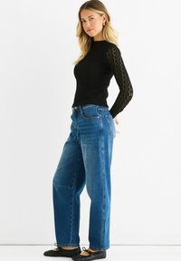 Black textured long-sleeve top paired with light blue high-waisted straight-leg jeans and black ballet flats. Model stands sideways.