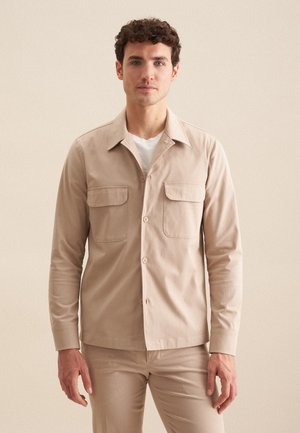 Lys beige skjorte med lange ærmer, to brystlommer og spids krave, lavet af et glat stof med en mat finish.