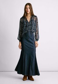 Blusa trasparente floreale con scollatura a V e dettaglio a cravatta, abbinata a una gonna svasata in denim scuro e stivaletti con tacco marroni.