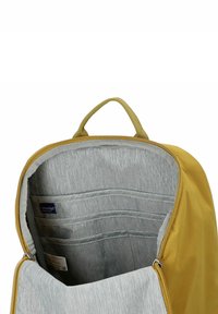 Zaino giallo con interno grigio. Presenta una maniglia superiore, chiusura a zip e diverse tasche interne con una finitura testurizzata.