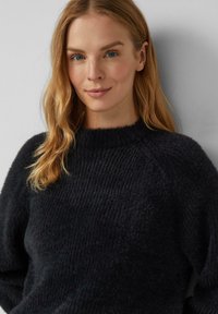 Czarny dzianinowy sweter o teksturowanym wykończeniu, z okrągłym dekoltem i luźnym krojem, wykonany z miękkiego, puszystego materiału.