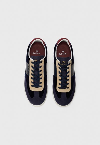 Sneakers Paul Smith navy e beige con lacci neri e soletta bordeaux, posizionati uno accanto all'altro su uno sfondo bianco.