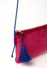 Borse a tracolla in velluto rosso con una tracolla intrecciata blu e un grande motivo con nappina blu. Presenta un dettaglio con zip dorata nella parte superiore.