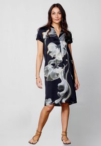 Vestido de manga corta, negro, con un estampado floral en blanco y dorado, de tela suave, hasta la rodilla, con un corte holgado, que presenta un cuello y detalles de botones.