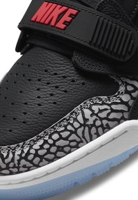 Baskets en cuir noir avec une semelle intermédiaire texturée grise et noire à motifs, un logo Nike rouge et une semelle extérieure en caoutchouc blanc.