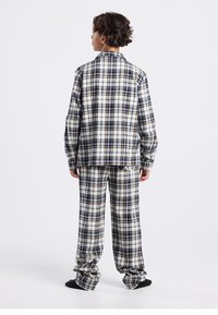 Checked flannel pajama set featuring a button-up shirt and matching pants in cream, navy, and brown colors, with long sleeves and relaxed fit.