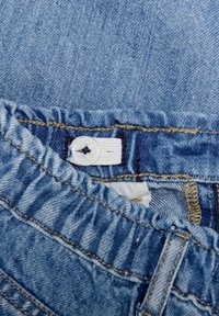 Denim kledingstuk met een elastische tailleband, lichtblauwe kleur en zichtbare stikseldetails. Voorzien van een witte knoop en een binnenlabel.