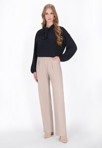 Blusa blu navy con dettaglio a fiocco, abbinata a pantaloni beige a pieghe. Tessuto liscio con vestibilità rilassata e silhouette a gamba larga. Tacchi dai colori neutri.