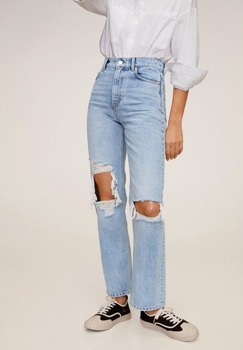 Jeans de tiro alto en azul claro con grandes rasguños en las rodillas, un corte relajado y bordes deshilachados, combinados con zapatillas negras y blancas.