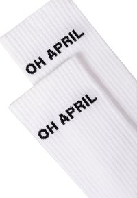 Calzini bianchi a coste con testo nero che recita "OH APRIL" lavorato nella parte superiore. Texture morbida e design casual.