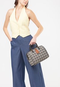 Borsa in tessuto nero e crema con motivo geometrico, dettagli in pelle e etichetta per bagagli; modello che indossa un top halter giallo chiaro e pantaloni ampi.