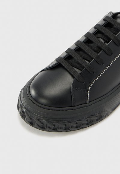 Baskets en cuir noir avec un bout arrondi, semelle en caoutchouc texturé, lacets plats et clous décoratifs en métal argenté le long de la couture latérale.