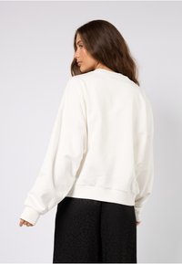 Felpa bianca con taglio morbido, spalle scese e polsini a coste, abbinata a una gonna nera con motivo.