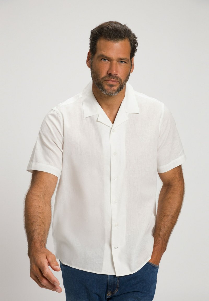 Chemise blanche à manches courtes avec boutons, fabriquée en tissu léger, présentant un col à revers et une texture lisse et propre. Associée à un jean bleu.
