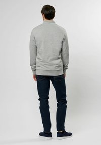 Grå sweatshirt med høy krage, ribbede mansjetter og nederkant, kombinert med mørkeblå jeans og marineblå sko, sett bakfra.