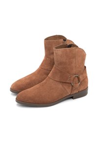 Botas de ante marrón hasta el tobillo con un acabado suave, punta afilada y una correa frontal que presenta un anillo de metal y botones decorativos. Suelas planas.