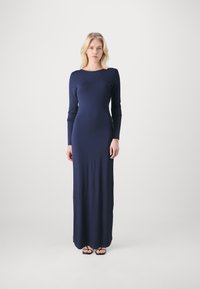 Navy long-sleeve gown made of smooth fabric, featuring a fitted silhouette, round neckline, and ankle-length design. Black sandals visible.