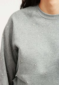 Felpa grigia con colletto rotondo e maniche raglan, decorata con borchie trasparenti sparse sulla parte frontale.