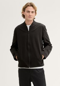 Czarna kurtka bombowiec z stójką, zamek błyskawiczny z przodu i długimi rękawami. Gładka tekstura, minimalistyczny design i boczne kieszenie.