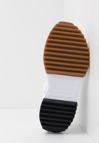 Semelle de chaussure avec une semelle à rainures en caoutchouc marron, blanc et noir, portant le nom de la marque "Converse" embossé sur la section blanche du milieu.