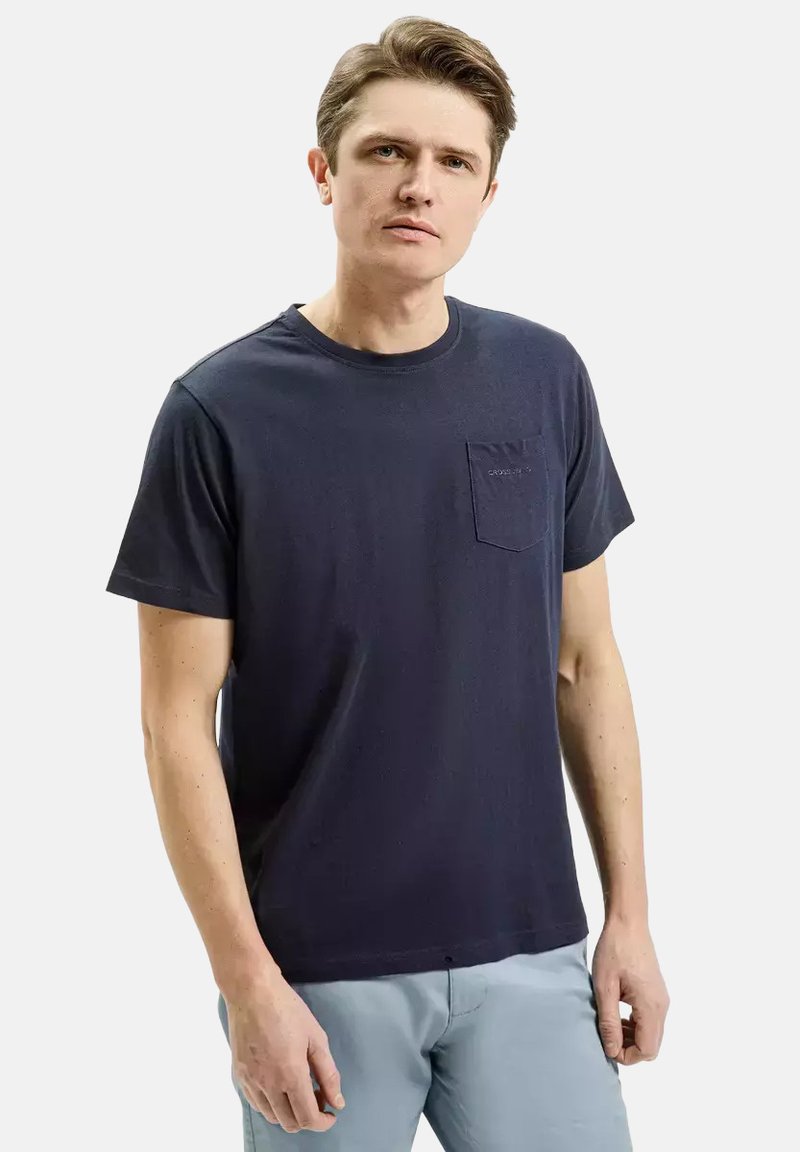 Granatowa koszulka z okrągłym dekoltem, wykonana z bawełny, z kieszonką na lewej piersi i krótkimi rękawami, o gładkiej fakturze i luźnym kroju.