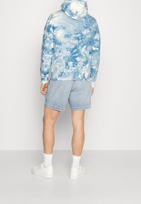 Hooded sweatshirt with a blue tie-dye pattern, paired with light denim shorts. White sneakers and crew-length socks complete the outfit.
