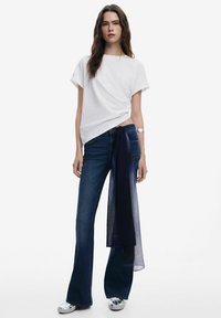 Hvid T-shirt med korte ærmer kombineret med mørkeblå farvede jeans med vidde og et marineblåt bælte bundet om taljen. Skinnende sølv sko fuldender looket.