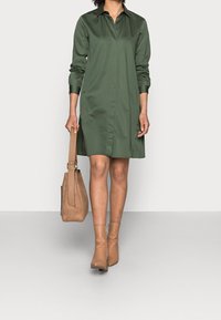 Grön knäppning klänning med lång ärm, gjord av slätt tyg. Matchad med en tan mockaväska och bruna ankelstövlar.