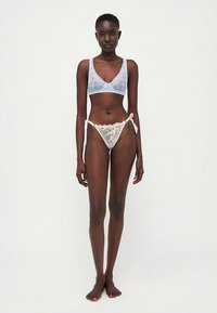 Lingerie set features a light blue sheer bralette with geometric patterns and a cream lace thong with ribbon ties.
