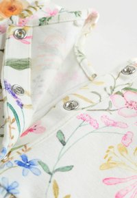 Lillelille trikoosärgid valge kangaga, millel on erinevaid värvilisi mustreid roosa, lilla ja sinise lilledega, hõbedased pressnupud ja pehme tekstuur.