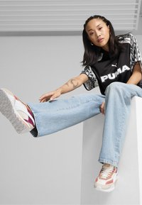 Maglietta grafica nera e bianca Puma, jeans in denim azzurro chiaro e sneakers multicolori con suole texture e dettagli in gomma.