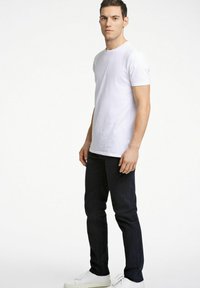 T-shirt in cotone bianco con colletto a girocollo, abbinato a pantaloni slim-fit blu scuro e sneaker bianchi. Design semplice, senza motivi o accenti.