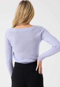 Suéter de punto en color púrpura claro con un amplio escote barco, mangas largas y acentos de canalé. Presenta una tela texturizada y una silueta ajustada.