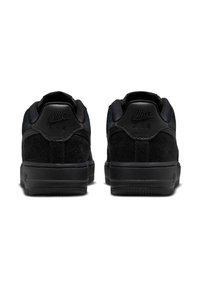 Melnā zamšādas zema profila kedas ar gludu melnu ādas papēdi. Iespēlēts Nike Air logo, mīksta apkakle un teksturēta gumijas zole.