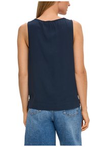 Top senza maniche blu navy con scollatura rotonda; tessuto liscio con vestibilità ampia, abbinato a jeans azzurri a vestibilità comoda.