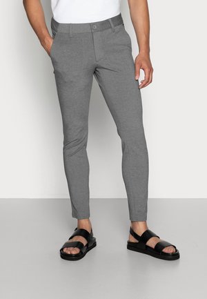 Pantalons extensibles gris à coupe slim, avec une fermeture à bouton et des poches latérales. Associés à des sandales noires à larges brides.
