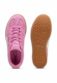 Růžové semišové tenisky Puma s tkaničkami, zobrazené z vrchu a s detailním fotografií gumové podrážky s kulatým vzorem.