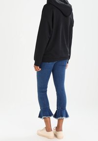 Svart hoodie, blå denim flare jeans med fransad nederkant och beige sneakers. Jeansen har en figurnära passform med midjehöjd.