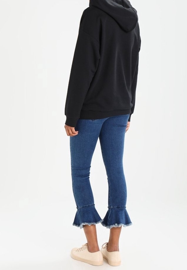 Svart hoodie, blå denim flare jeans med fransad nederkant och beige sneakers. Jeansen har en figurnära passform med midjehöjd.