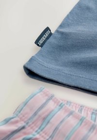 Modrá bavlněná tričko s přeloženým rukávem a štítkem "Superdry"; pod ním je látka s růžovými a modrými pruhy, která naznačuje šortky.