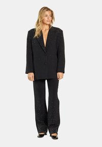 Conjunto negro con un blazer de escote en V profundo y pantalones de pierna ancha, que presentan adornos de pedrería dispersos y una textura de tela suave.