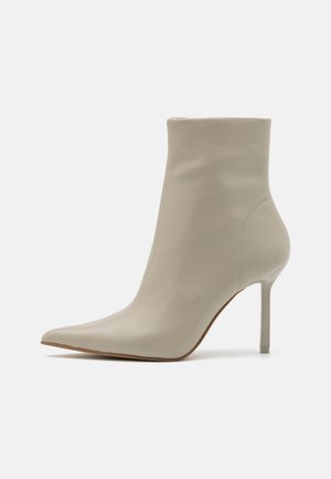 Beige læderankelstøvle med spids tå og slank høj hæl på enkel lys baggrund.
