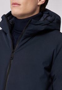 Marineblaue Kapuzenjacke mit glatter, matter Oberfläche und hohem Kragen, ausgestattet mit einem schwarzen Reißverschluss und verstellbaren Kordeln an der Kapuze.