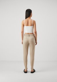 Beige gestreepte broek met een elastische tailleband en twee achterzakken, gecombineerd met een witte getailleerde top met dunne bandjes.