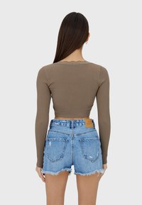 Langarm ribgebreide top in taupe, gecombineerd met versleten denim shorts met rafelige zomen en een bruine leren label aan de achterkant.