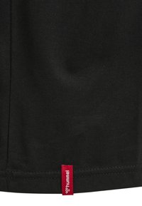 Czarny bawełniany t-shirt o prostym kroju, z małą czerwoną metką "hummel" umieszczoną przy dolnym szwie. Gładka tekstura, minimalistyczny design.